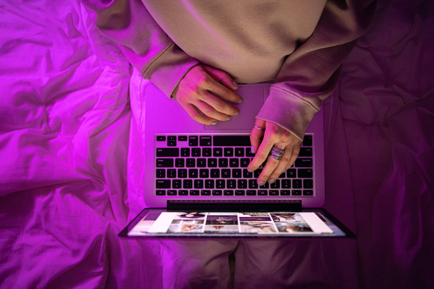 Person mit Laptop auf dem Schoß, tippt auf der Tastatur, lila Licht beleuchtet Decke und Hände.