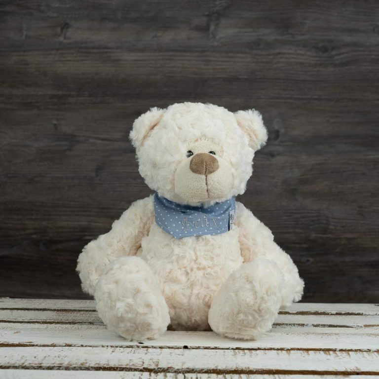 Weißer Teddybär mit blauer Halstuch-Schleife und „Felix“-Stickerei auf rustikalem Holztisch.