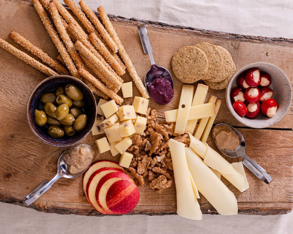 Unverschwendet Performance Marketing 4 Rustikale Brettljause auf Holzbrett mit Käse, Obst, Nüssen und Dips aus Unverschwendet-Produkten fein angerichtet.