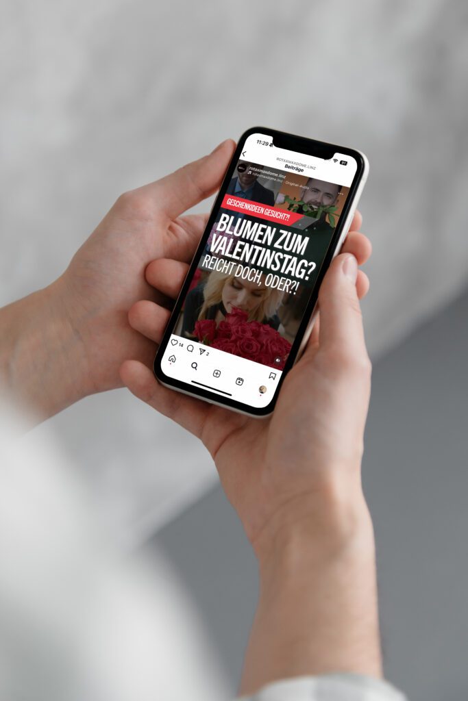 Person hält Smartphone mit Instagram-Post der Rotax MAX Dome Kampagne zum Valentinstag mit Text: „Blumen zum Valentinstag? Reicht doch, oder?!“