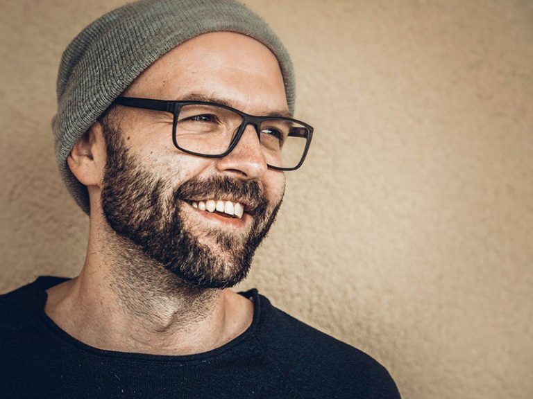 Markus Strengberger 4 Porträt eines herzlich lachenden Mannes mit Vollbart, schwarzer Brille und grauer Mütze, der zur Seite blickt