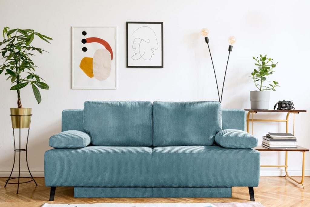 Möbel Polt Online Marketing 5 Hellblaues Sofa vor weißer Wand mit modernen Bildern, Zimmerpflanzen und minimalistischer Einrichtung im Wohnzimmer.