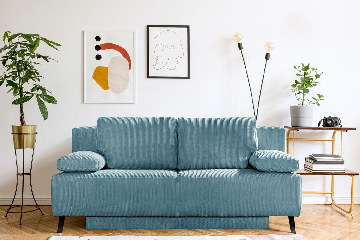 Hellblaues Sofa vor weißer Wand mit modernen Bildern, Zimmerpflanzen und minimalistischer Einrichtung im Wohnzimmer.