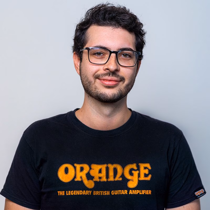 Julian Urban-Slabina 3 Porträt eines lächelnden jungen Mannes mit Brille, dunklen Haaren und Bart, der ein schwarzes T-Shirt trägt.