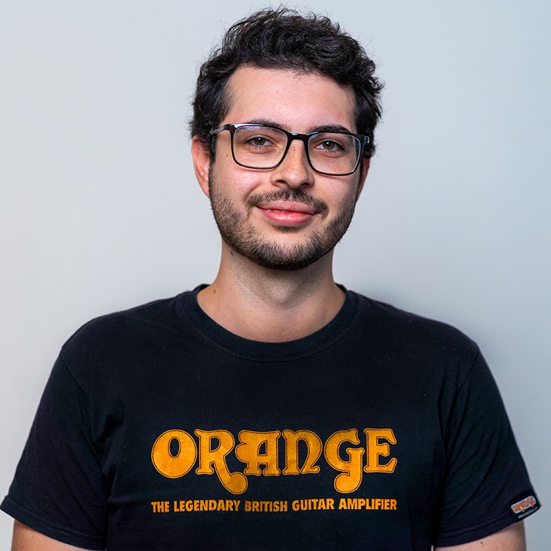 Porträt eines lächelnden jungen Mannes mit Brille, dunklen Haaren und Bart, der ein schwarzes T-Shirt trägt.