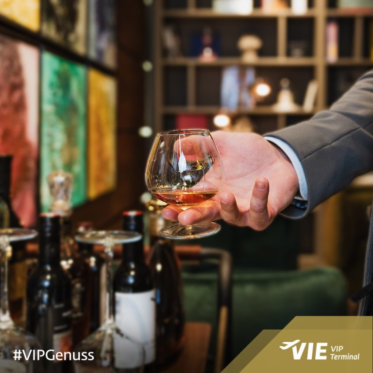 Social Media & Content Marketing für VIP Terminal Vienna Airport 4 Person im Anzug hält ein Glas Cognac oder Whisky, im Hintergrund Barwagen mit Flaschen im VIP Terminal Wien.