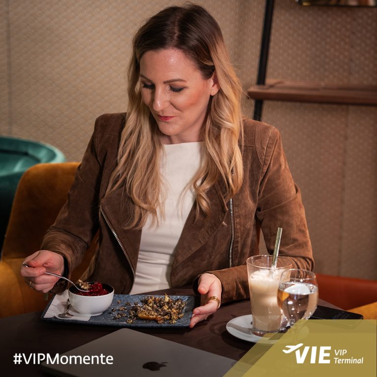 Social Media & Content Marketing für VIP Terminal Vienna Airport 8 Frau genießt Dessert mit Kaffee im VIP Terminal Wien, vor ihr ein Teller mit Crumble und Beeren, dazu Latte und Wasser.