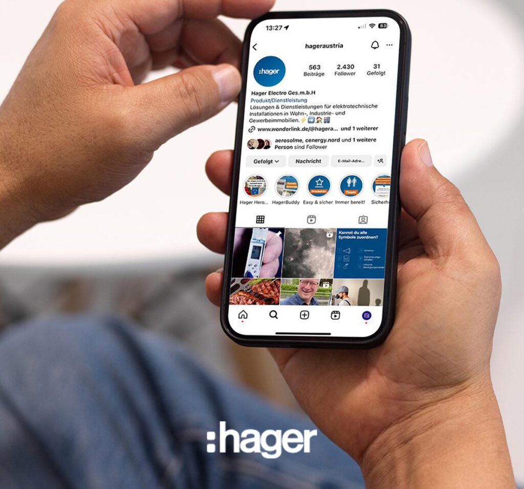 Person hält Smartphone mit geöffneter Instagram-Seite von @hageraustria, Hager-Logo unten im Bild sichtbar.