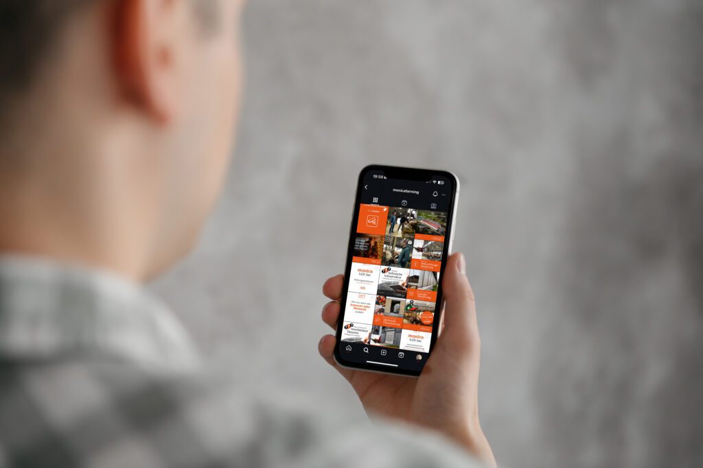Person hält Smartphone mit geöffnetem Instagram-Profil von @monicafarming, sichtbar sind mehrere orange-weiße Feed-Posts zur Landwirtschaft.