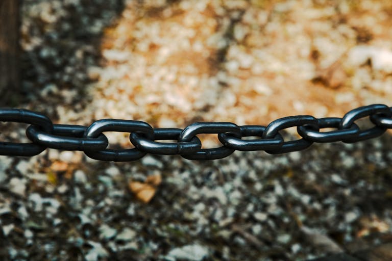 Detailed view of a sturdy black metal chain outdoors on a blurred background.